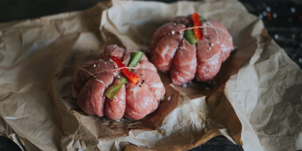Two parcels of meat with fresh produce stuffed inside, sat on brown paper.